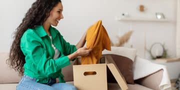 Happy Woman Holding Clothes Unpacking Cardboard Box At Home